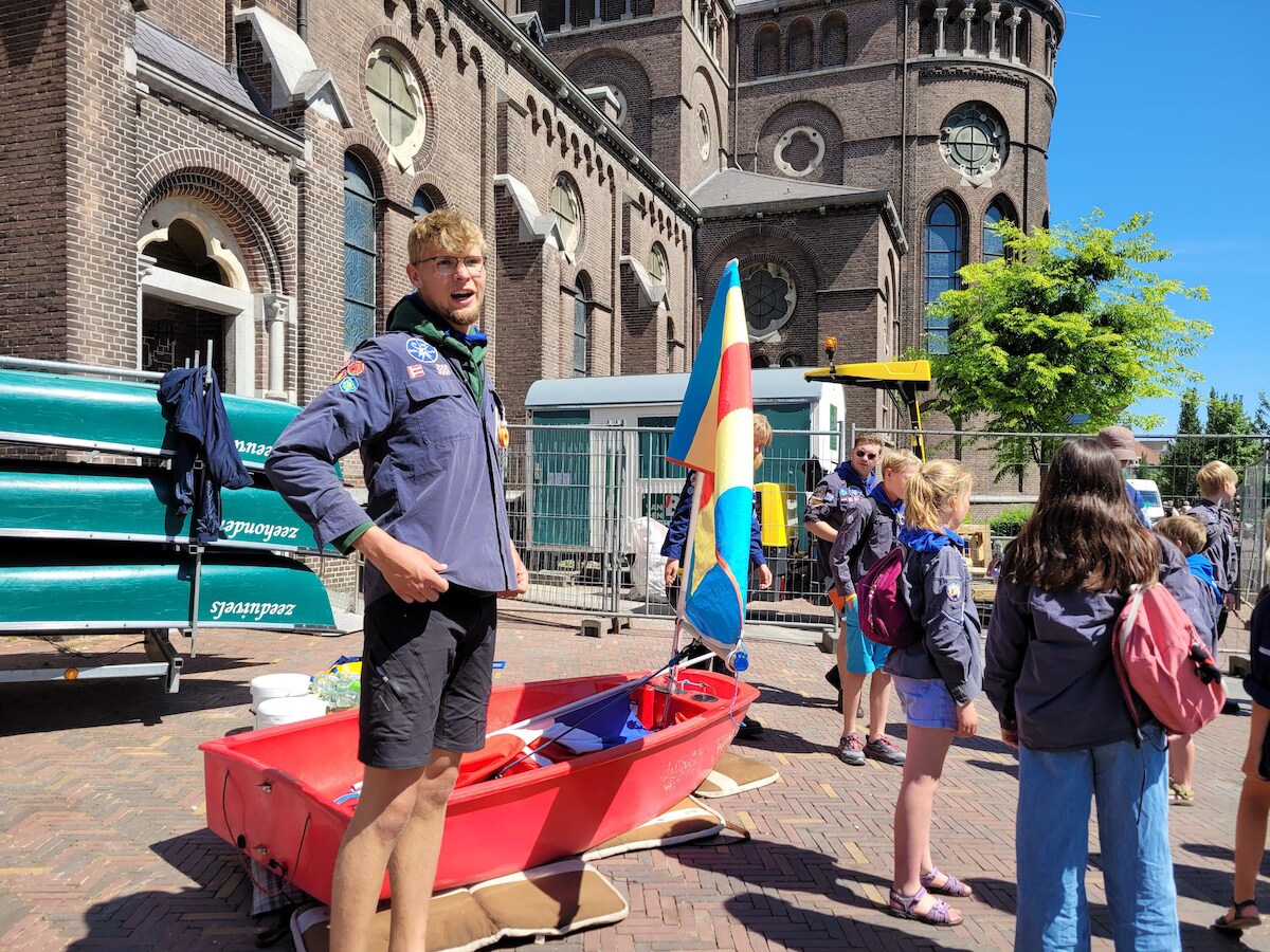Waterscouting gaat over land naar de kerk met een kleine zeilboot ...